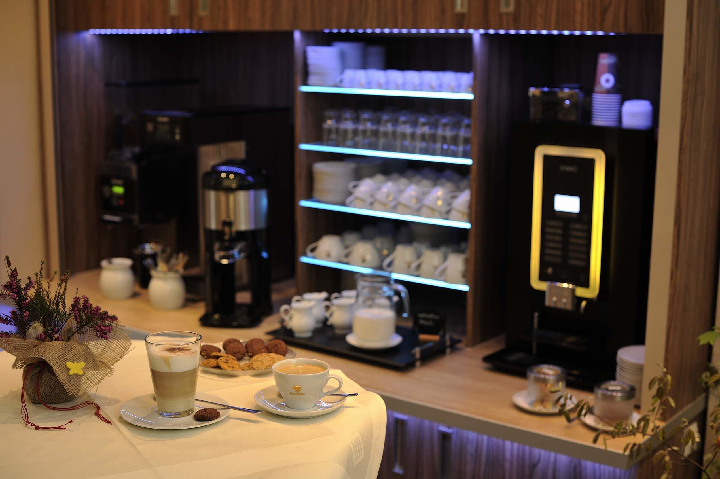 A coffee station with a coffee machine, cups, and a tray of cookies.