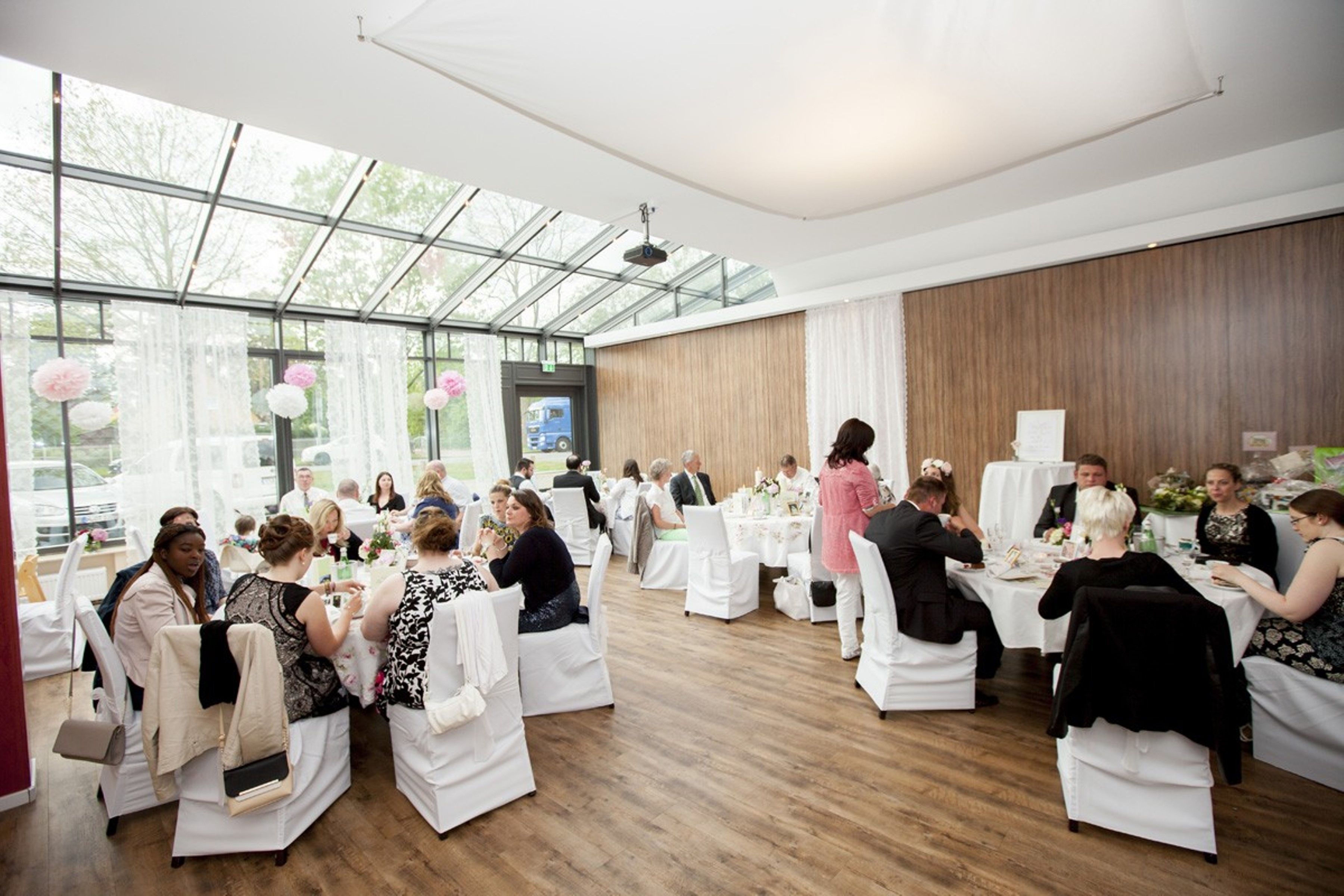 Un vaste espace intérieur doté de hauts plafonds et de grandes fenêtres, aménagé avec des tables et des chaises blanches, idéal pour l’organisation d’événements.
