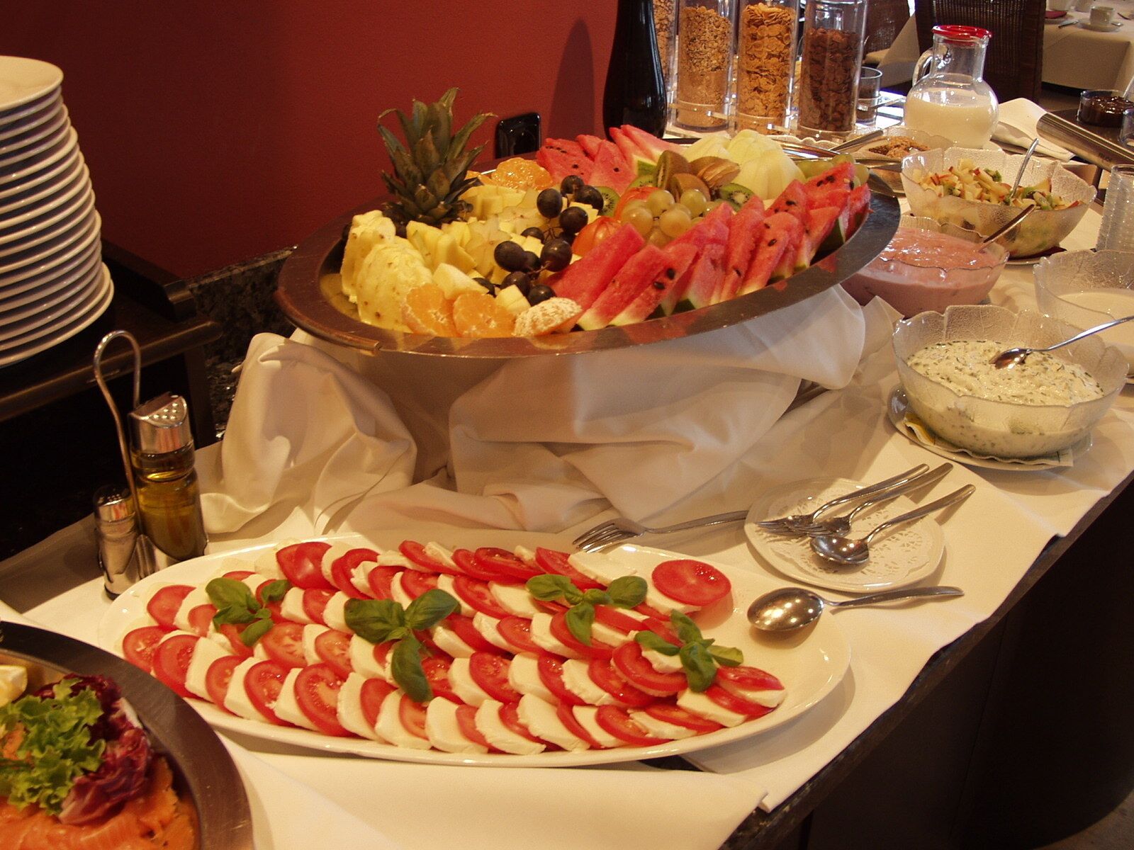 A buffet with various fruits, a salad, and a bowl of soup.
