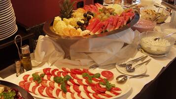A buffet with various fruits, a salad, and a bowl of soup.