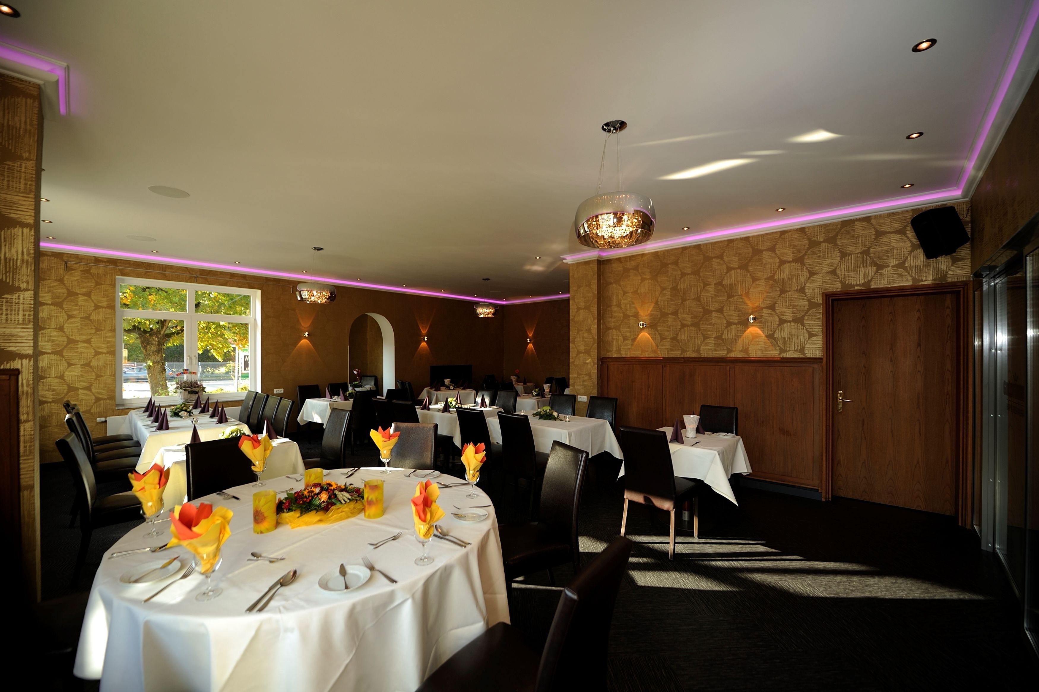 A dining area with round tables, chairs, and a chandelier.