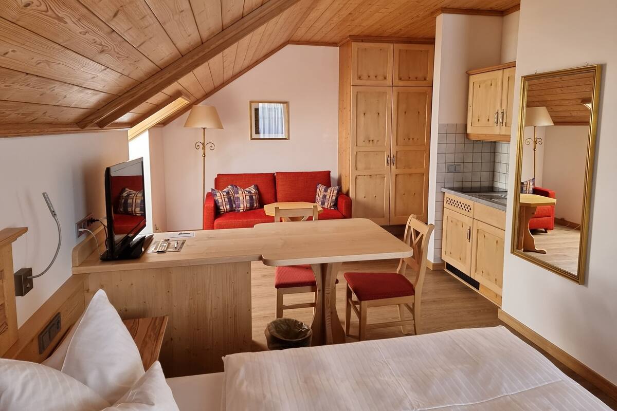 Um quarto aconchegante com teto de madeira, um sofá vermelho, uma mesa de jantar de madeira e uma área de cozinha com armários de madeira.