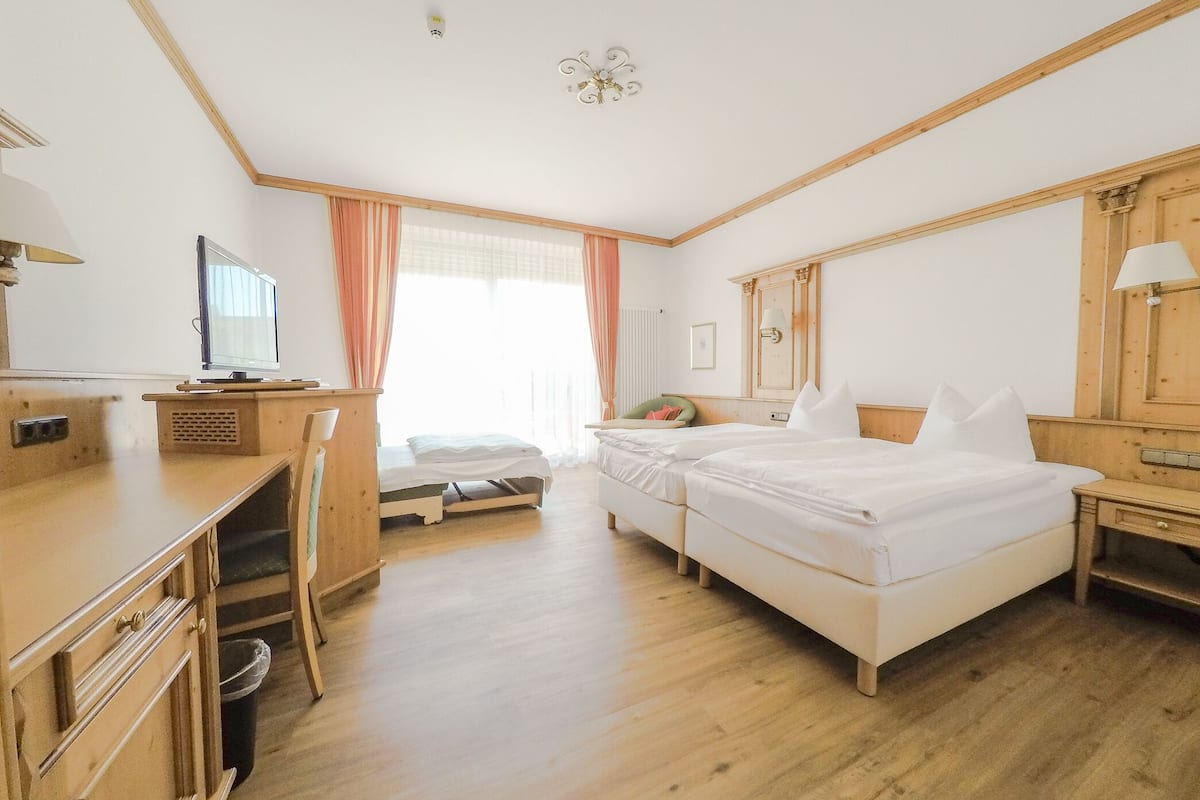 Quarto de hotel com escrivaninha de madeira, uma cama, uma mesinha e uma televisão.