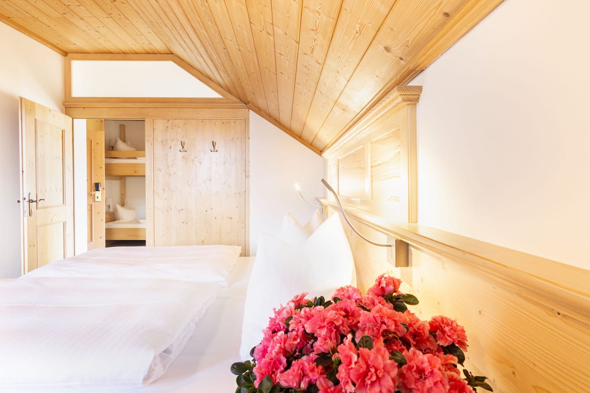 Quarto com teto de madeira, cama com roupa de cama branca e um arranjo floral rosa grande.