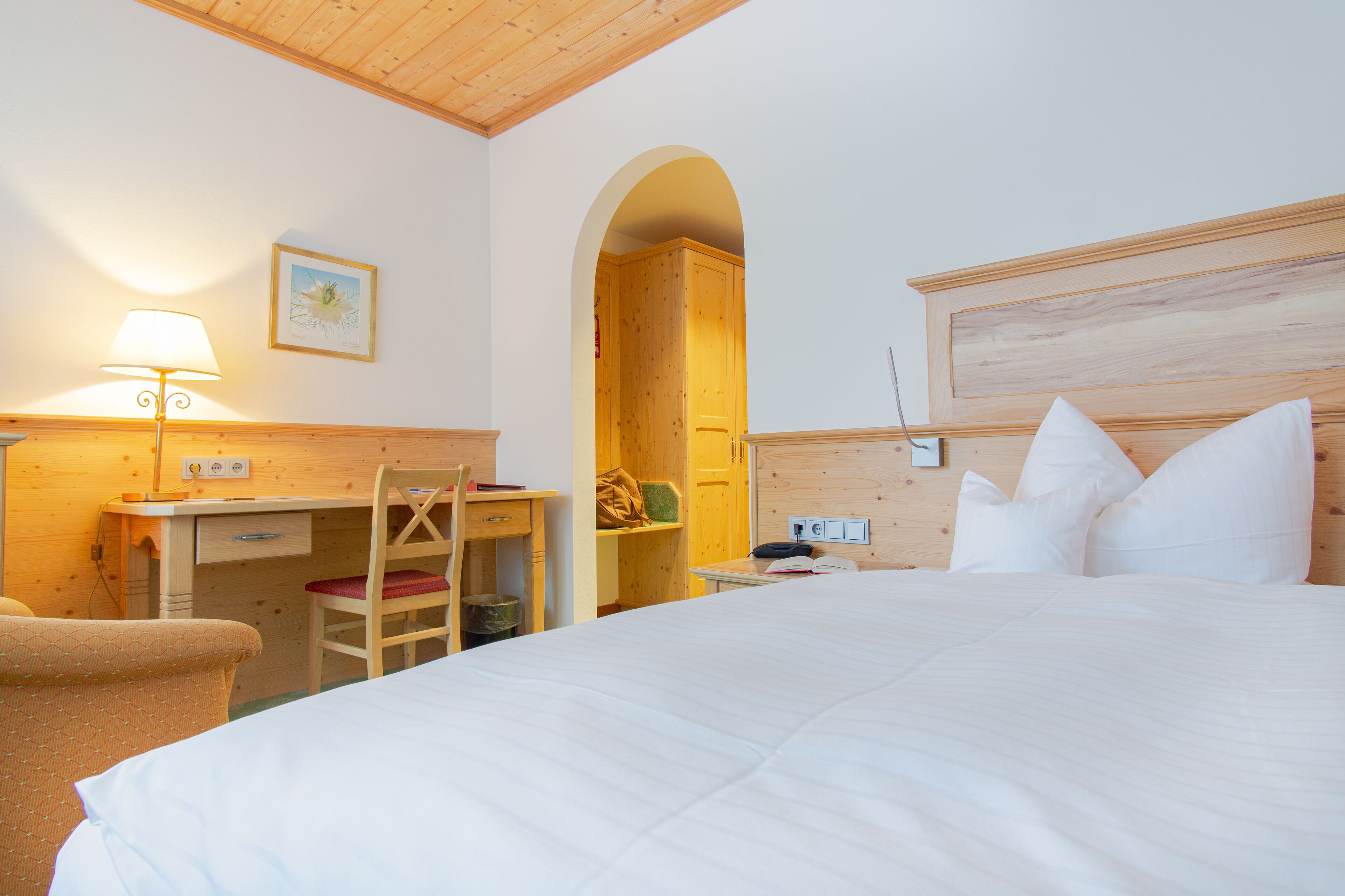Ein Schlafzimmer mit Bett, Schreibtisch, Stuhl und einem rundbogigen Durchgang.