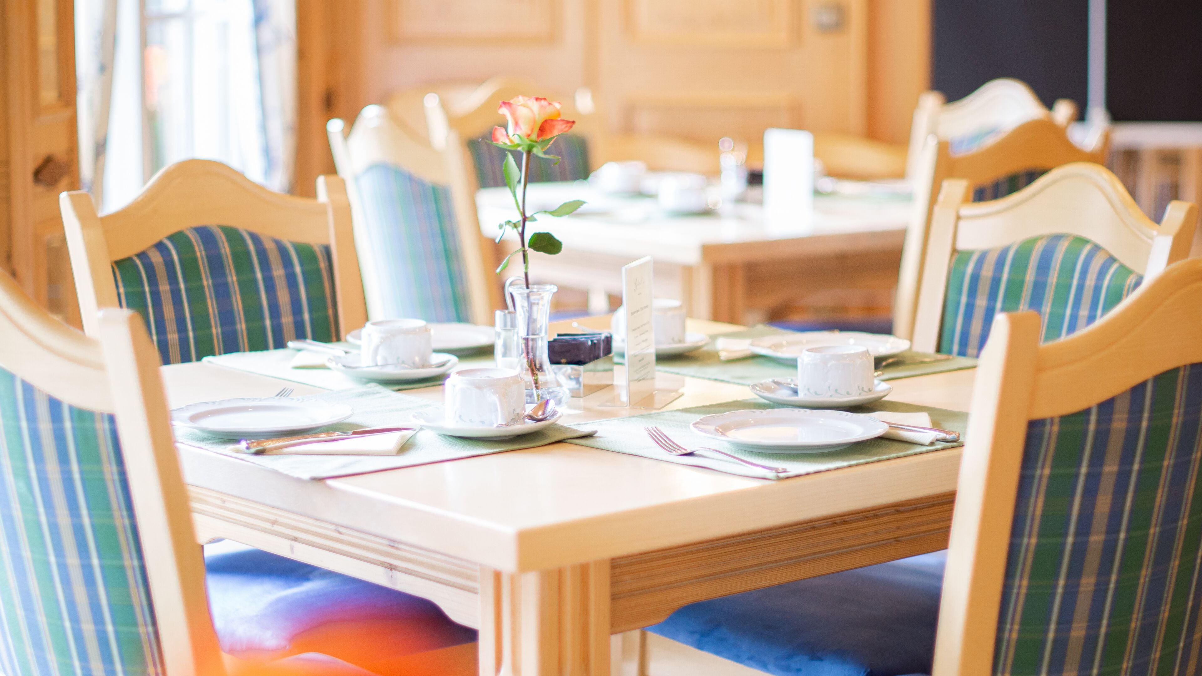 A dining table set for four with striped chairs, a vase with a single flower, and a menu stand.