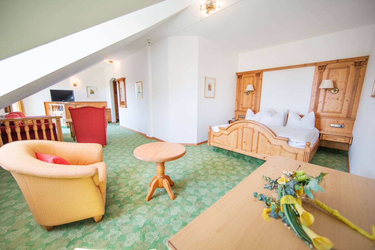 Quarto de hotel com cama, poltrona vermelha, mesa de madeira e uma mesinha redonda.