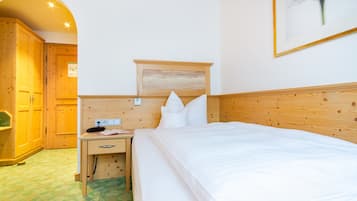 Habitación de hotel con cabecera de madera, cama con ropa blanca, mesita de noche con un teléfono y un libro, y un cuadro en la pared.