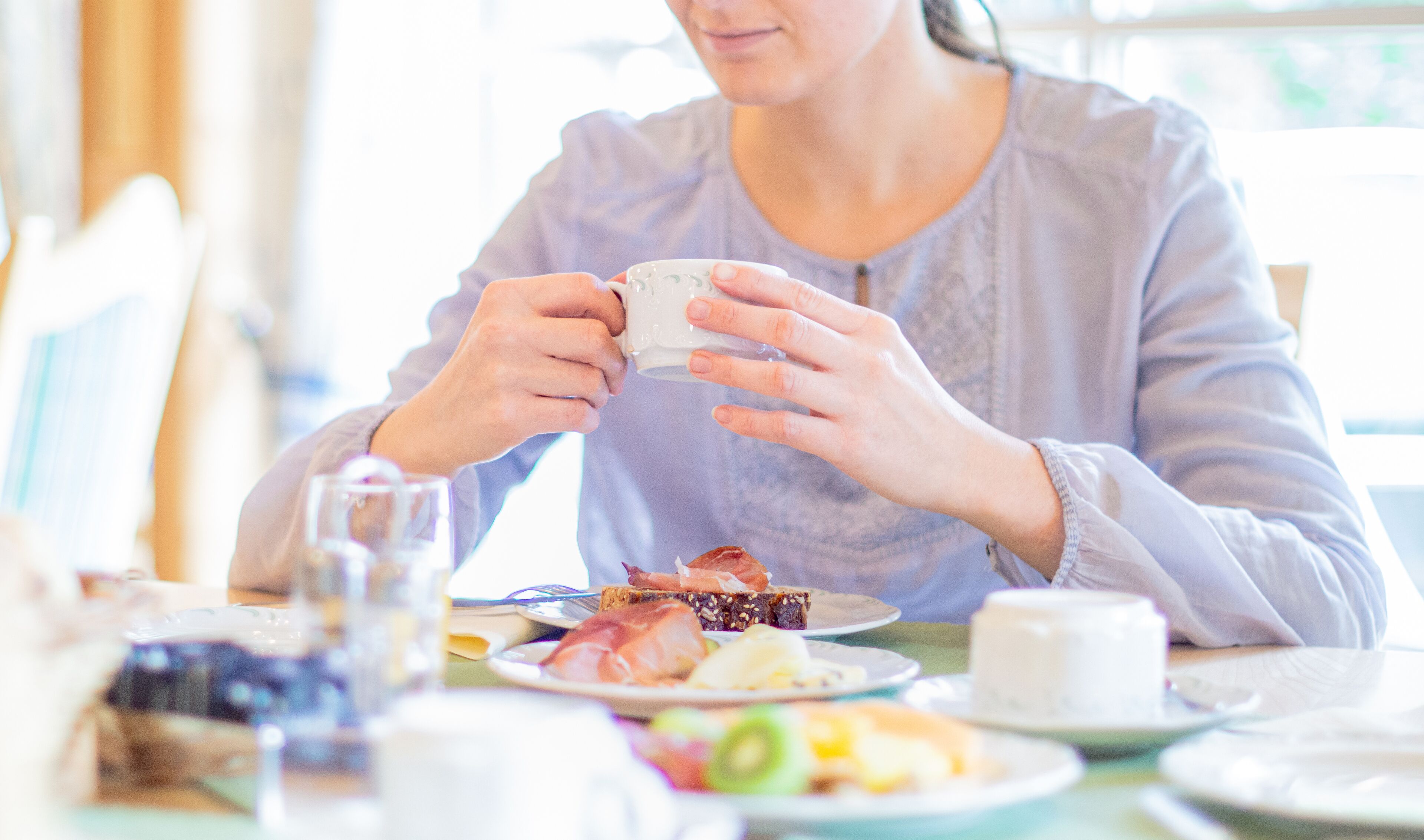 A person sitting at a table with a meal, including a cup, bread, and various food items.