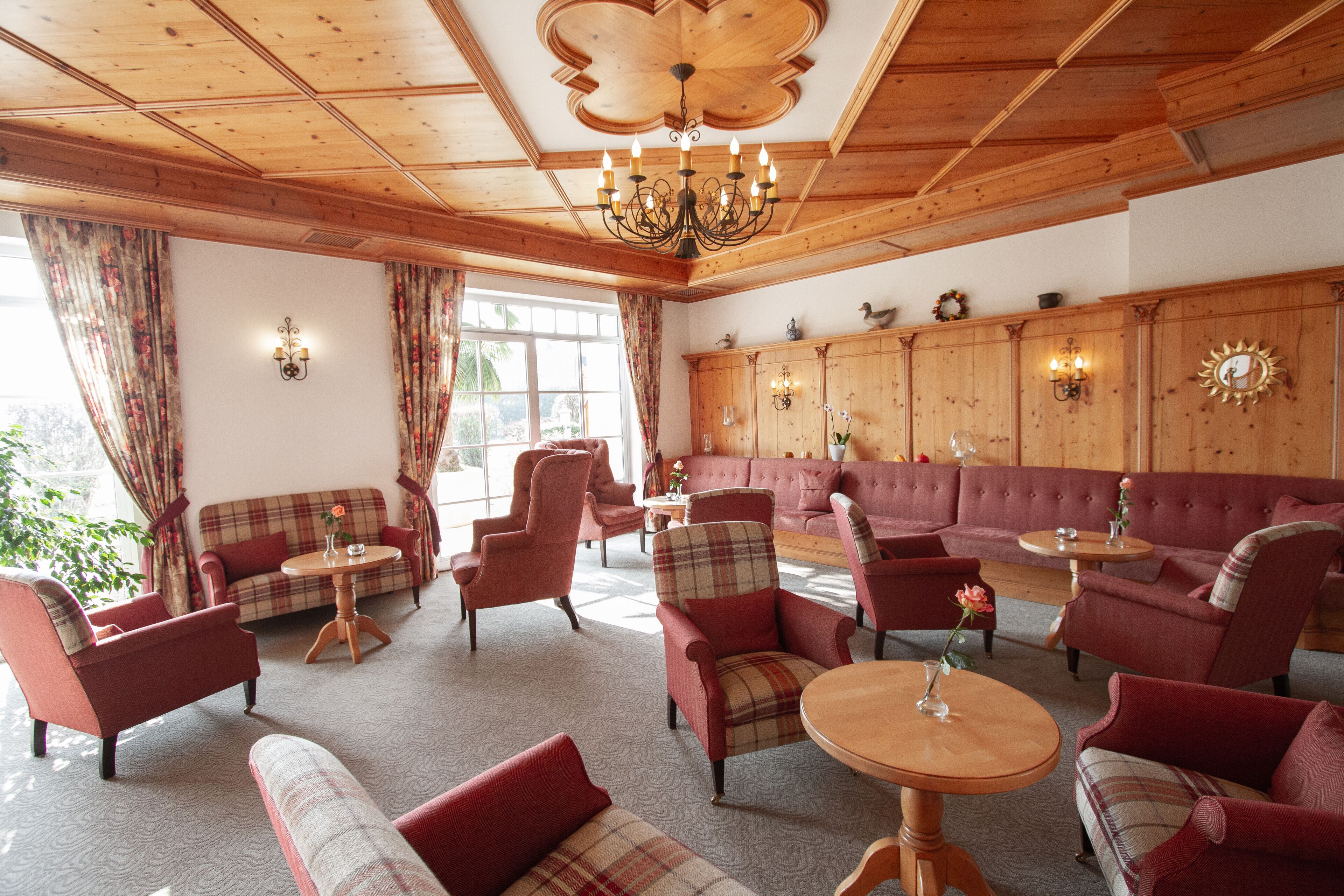 A cozy room with wooden ceilings, a large sofa, multiple armchairs, and a chandelier.