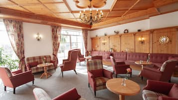 A cozy room with wooden ceilings, a large sofa, multiple armchairs, and a chandelier.