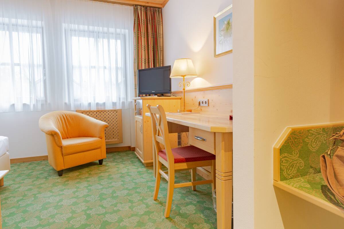Quarto de hotel com escrivaninha de madeira, televisão, luminária, cadeira e cama.