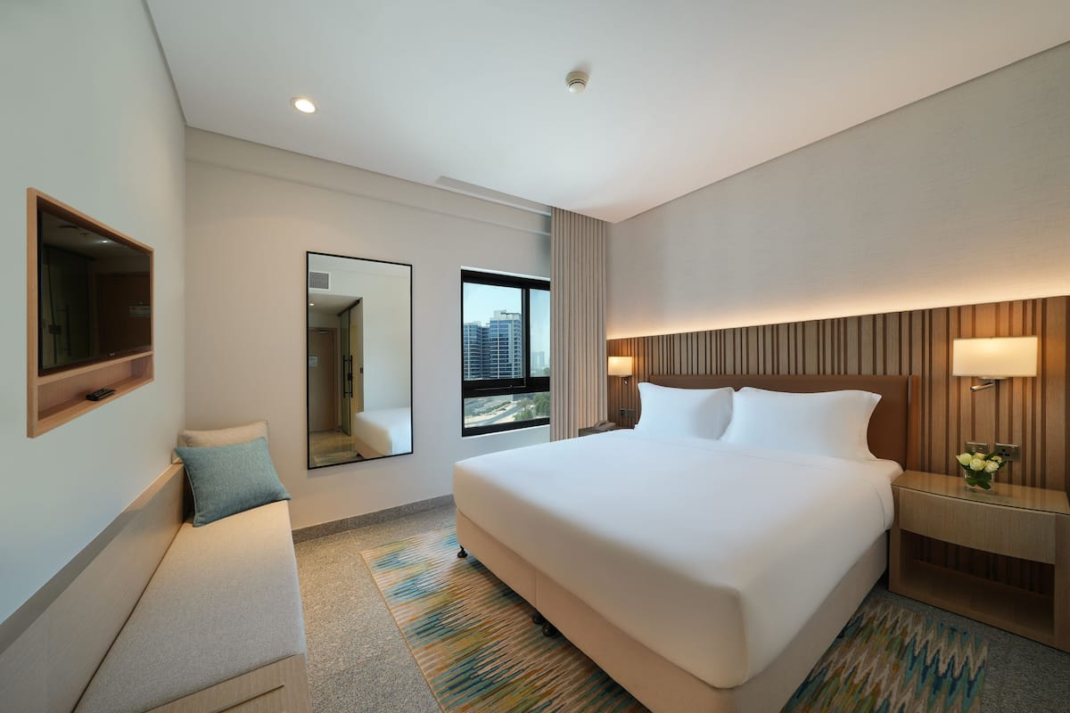 Ein Hotelzimmer mit einem großen Bett, einem Nachttisch, einem Spiegel und einem Fenster mit Blick auf die Stadt.