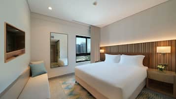 A hotel room with a large bed, a bedside table, a mirror, and a window with a city view.