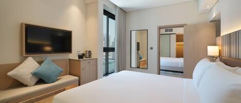 Une chambre d’hôtel moderne dotée d’un grand lit, d’un téléviseur à écran plat, d’un coin salon avec une machine à café et offrant une vue sur la ville par la fenêtre.