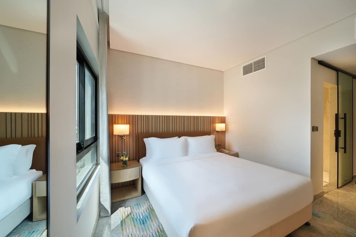 Ein Hotelzimmer mit einem großen Bett, Nachttischen, einem Fenster und einer Tür.