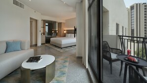 A modern hotel room with a balcony, a sofa, a dining table, and a view of the cityscape.