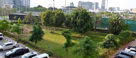 A parking lot with multiple cars, a grassy area with trees, and a city skyline in the background.
