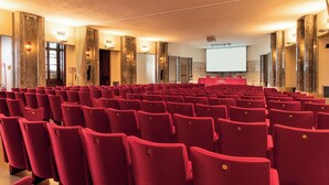 A conference room with rows of red chairs, a projection screen, and marble pillars. - Villa Fenaroli Palace Hotel (Rezzato)