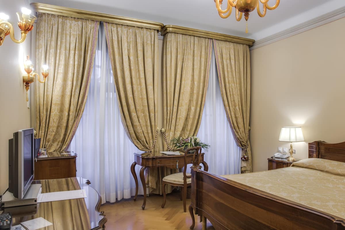A hotel room with a large bed, a desk with a computer, a chair, a lamp, and curtains.
