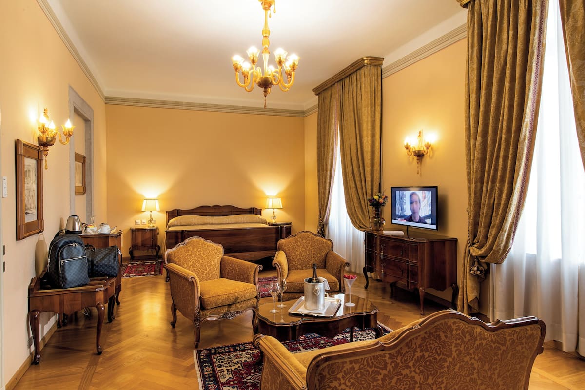 A hotel room with a bed, two armchairs, a coffee table, a television, and a desk with a lamp.