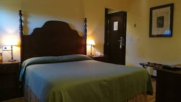 Una habitación de hotel con una cama grande, dos mesitas de noche con lámparas, una puerta de madera y un cuadro en la pared.