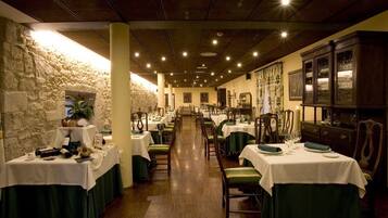 A restaurant with tables set for dining, a stone wall on one side, and a wooden cabinet on the other.