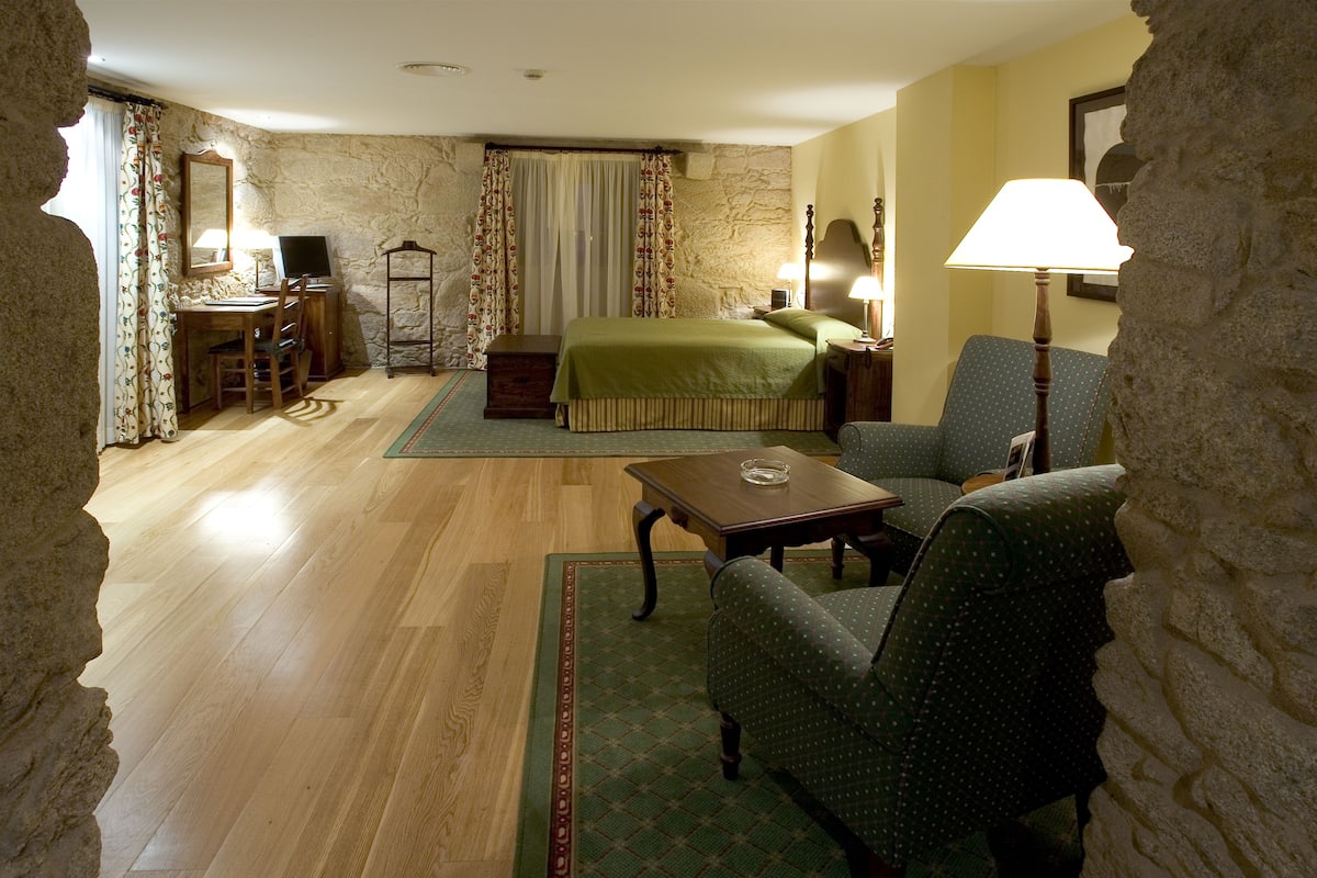 Una habitación con cama, escritorio, silla, lámpara y espejo.
