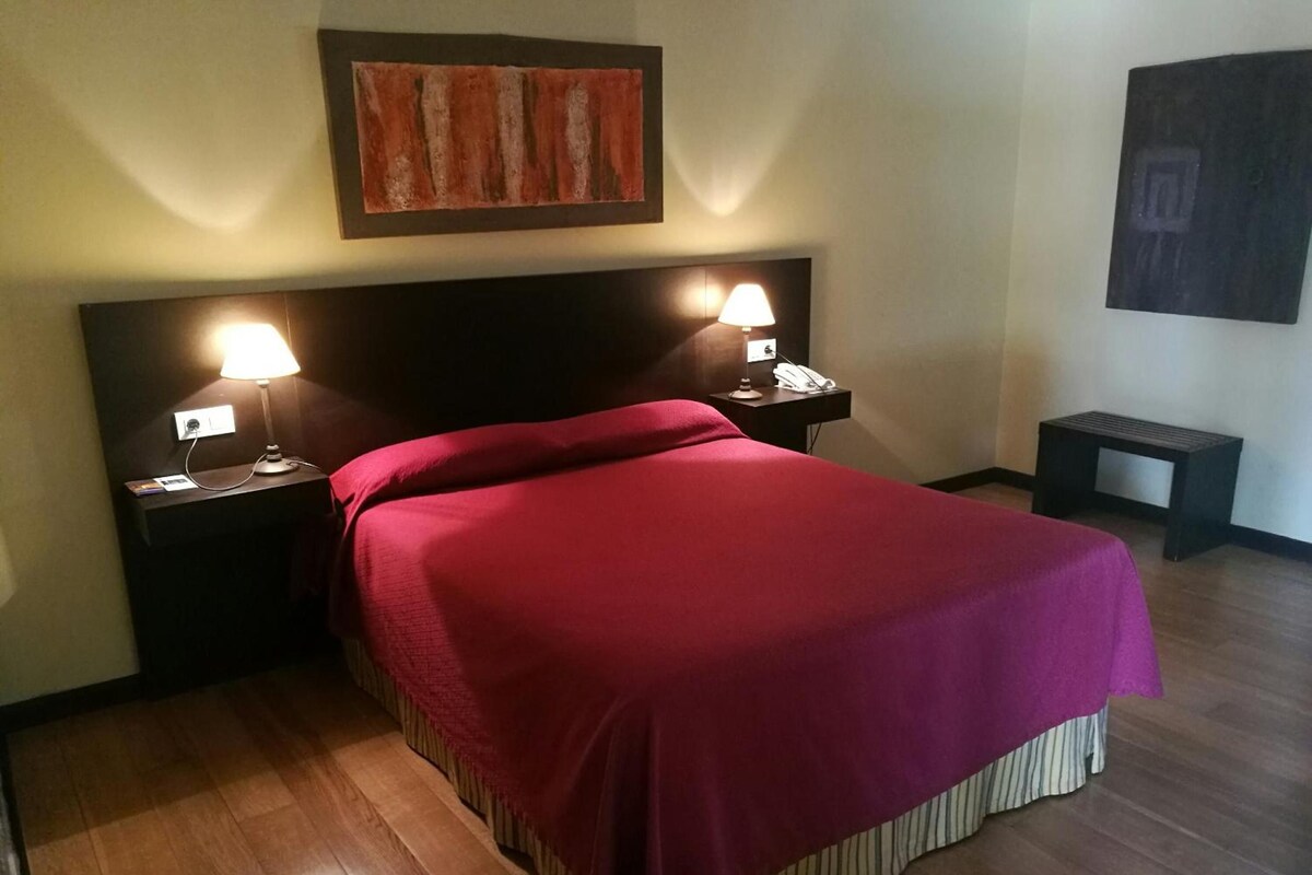 Habitación de hotel con una cama grande, dos lámparas de noche, una mesita de noche y un cuadro en la pared.