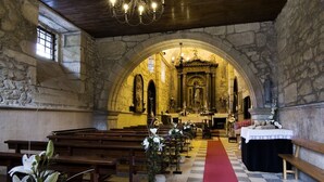 Interior de una iglesia con paredes de piedra, bancos de madera, una alfombra roja que conduce al altar y arreglos florales.