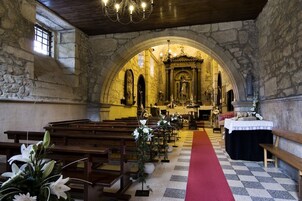 An interior of a church with stone walls, wooden pews, a red carpet leading to the altar, and floral arrangements.