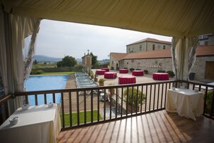 Una terraza con mesas y sillas, una piscina y vistas a un edificio con una cruz en la parte superior.