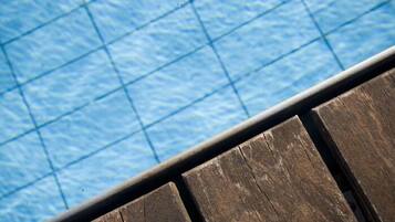 A wooden deck edge with a pool in the background.