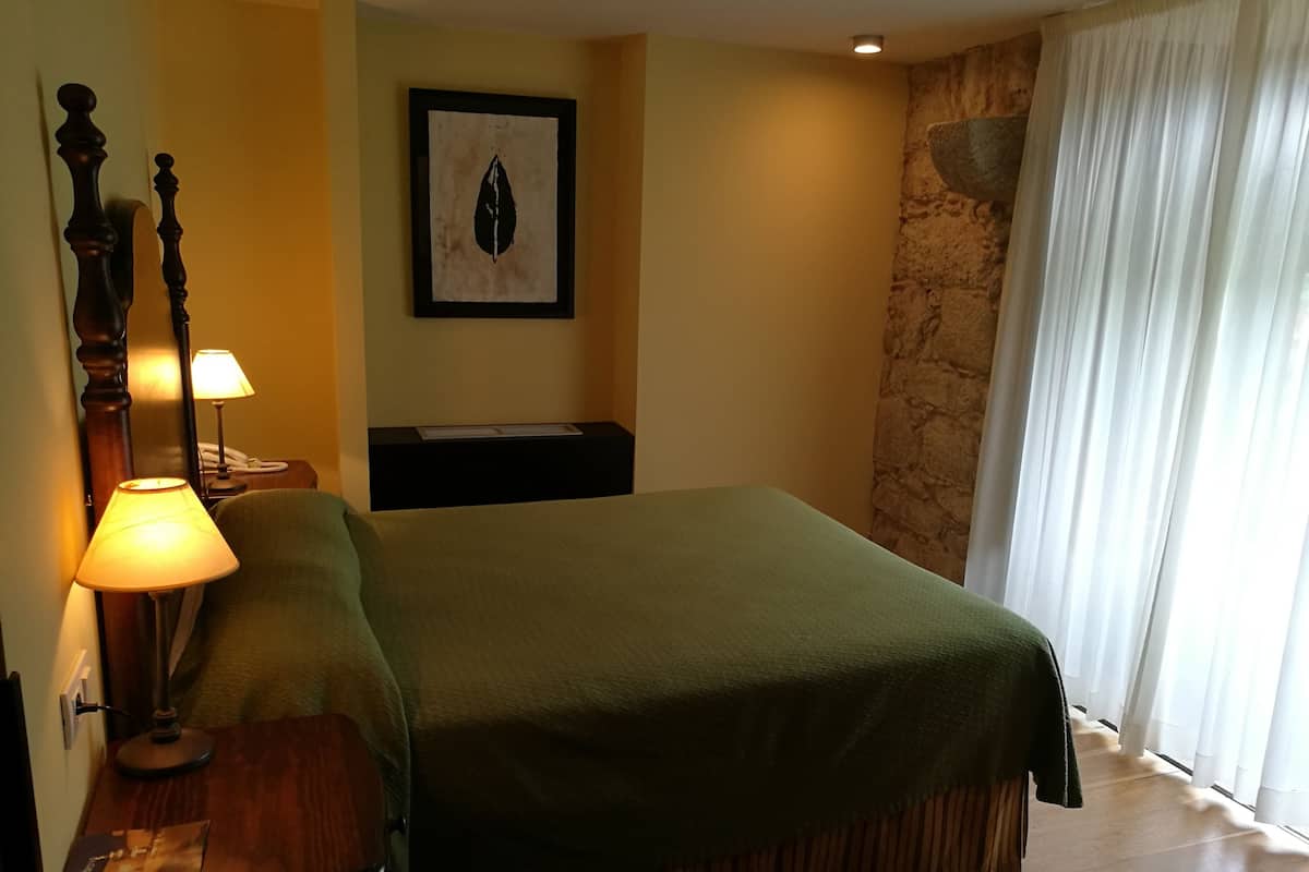 Una habitación de hotel con una cama, una mesita de noche con lámpara, un cuadro en la pared y una pared decorativa de piedra.