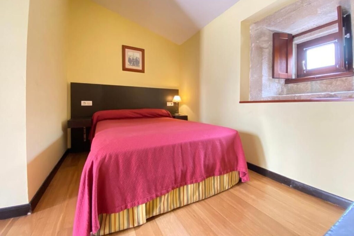 Una cama individual con cabecera, una lámpara de noche y una ventana con marco de madera.