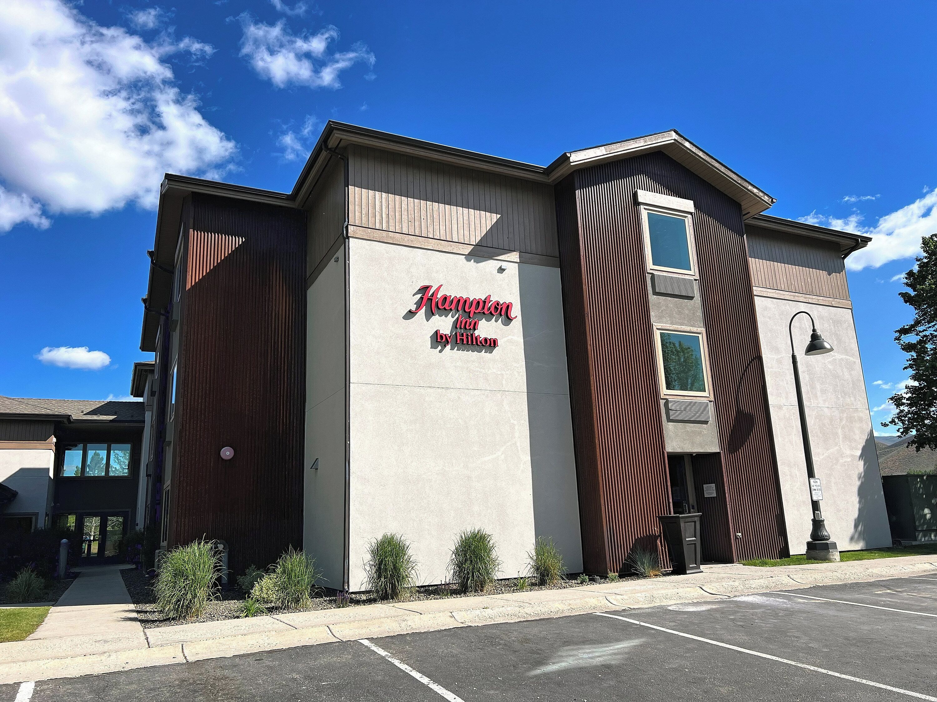A building with a sign reading 'Hampton Inn by Hilton' and a parking lot in front.