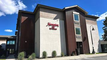 A building with a sign reading 'Hampton Inn by Hilton' and a parking lot in front.