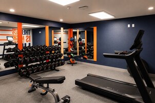 Un gimnasio con cinta de correr, mancuernas y pelotas de ejercicio.
