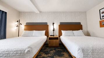 A hotel room with two beds, a nightstand, a lamp, and a patterned carpet.
