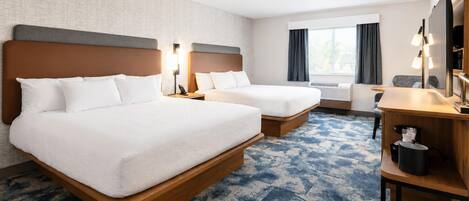 A hotel room with two beds, a desk, a chair, a lamp, and a window with curtains.