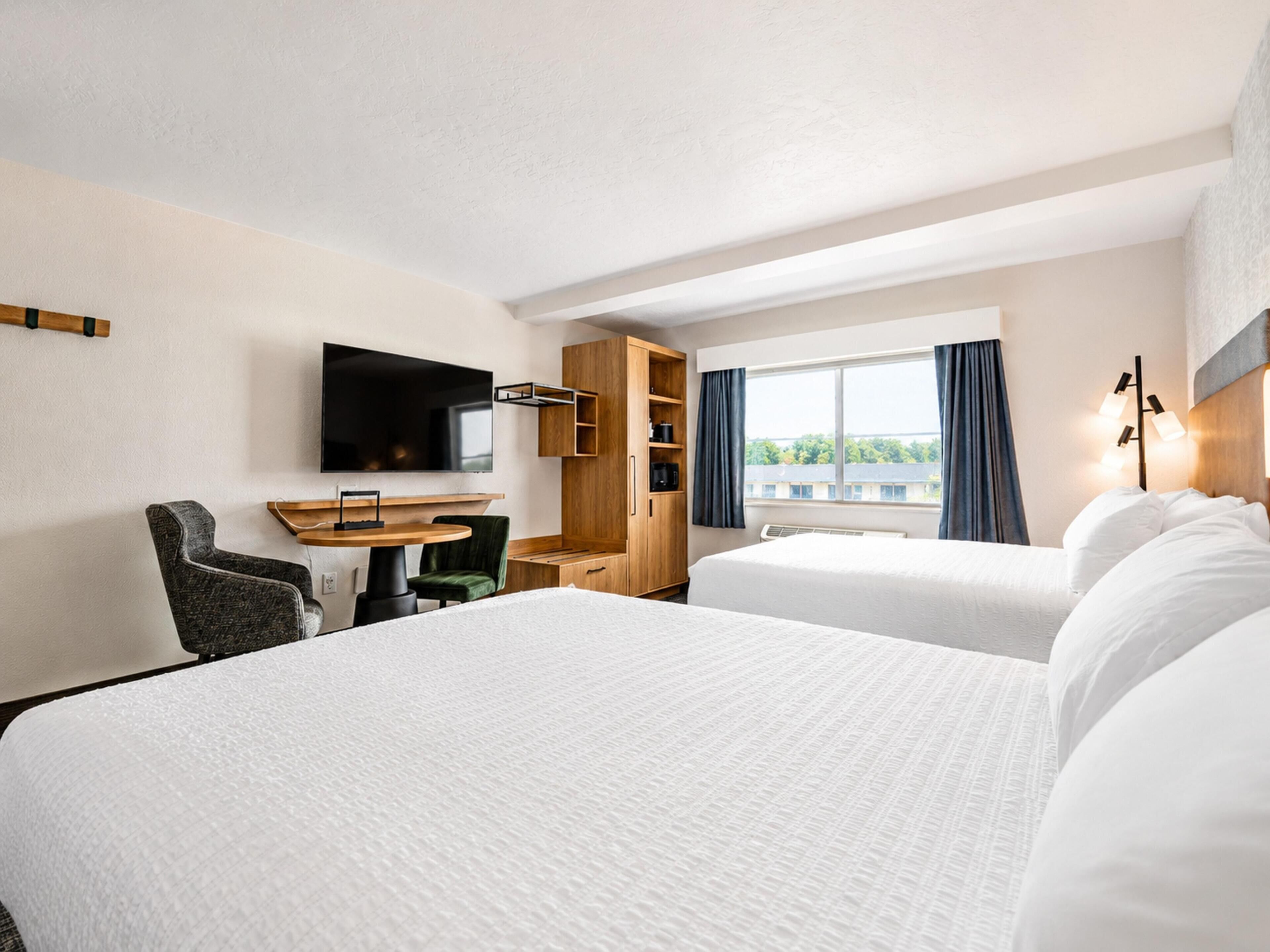A hotel room with two beds, a desk, a TV, and a window with curtains.