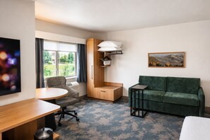 A hotel room with a green sofa, a wooden cabinet, a small table, a chair, and a painting on the wall. - Hampton Inn by Hilton Hailey Sun Valley (Hailey)