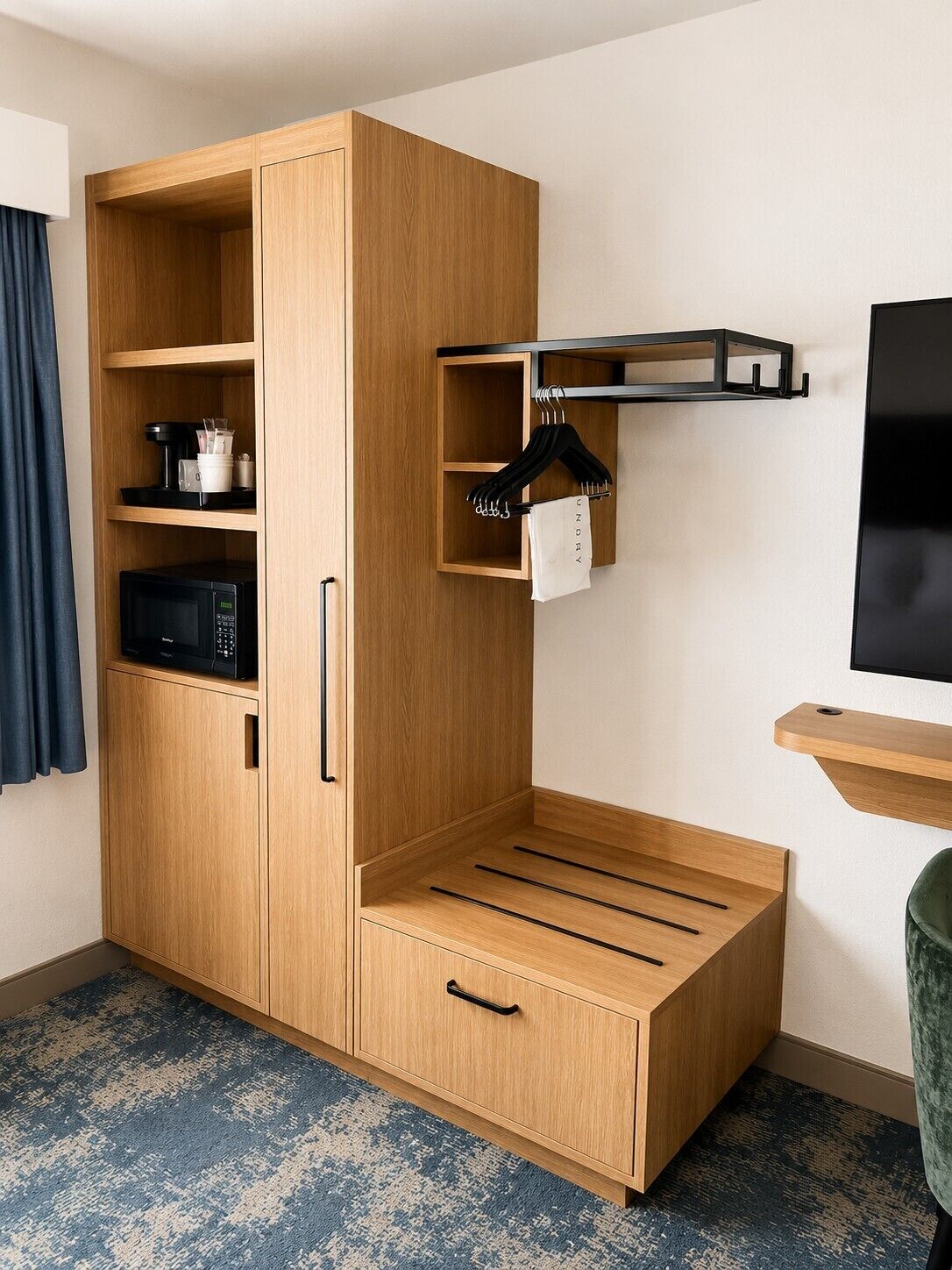 A compact room with a wooden wardrobe, a microwave, a TV, and a small shelf with hangers.