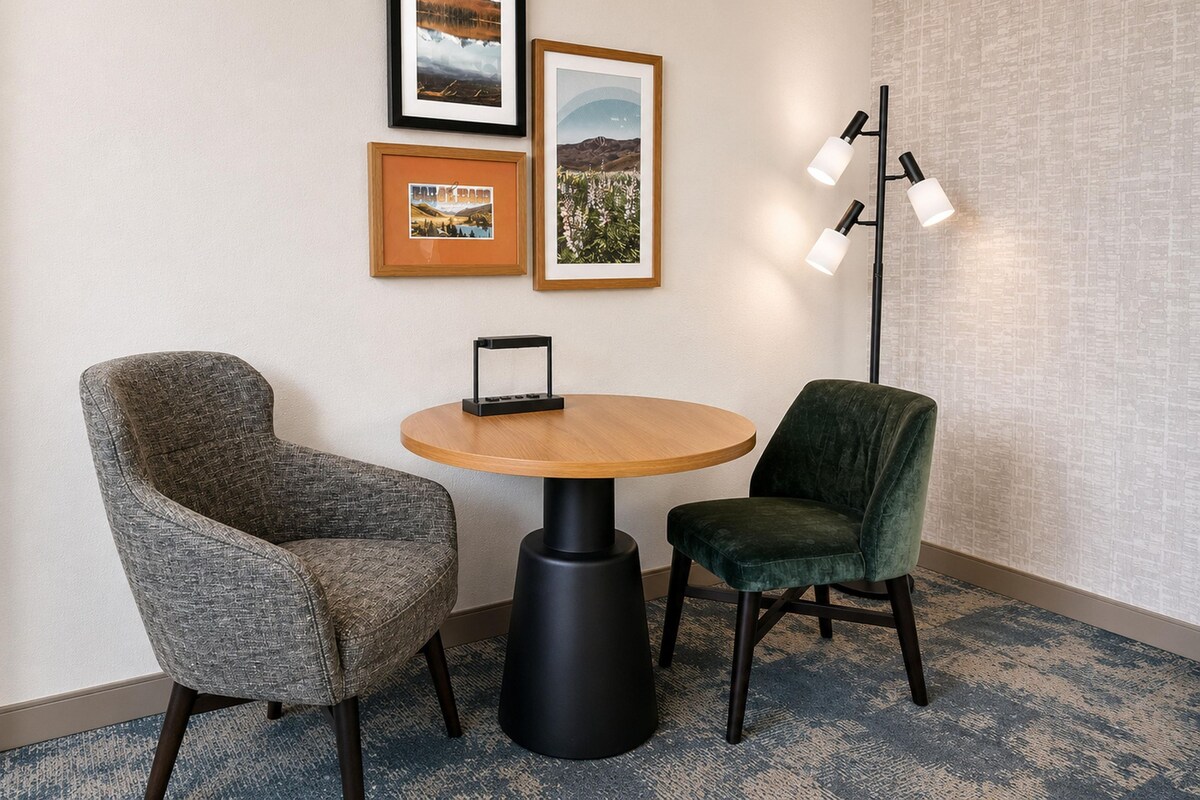 A room with a round table, two chairs, framed pictures on the wall, and a floor lamp.