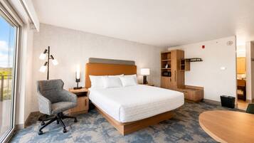 A hotel room with a bed, a desk, a chair, a lamp, and a view of the outdoors.
