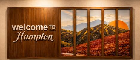 A welcome sign with 'welcome to Hampton' and a scenic landscape with mountains and a sunset.