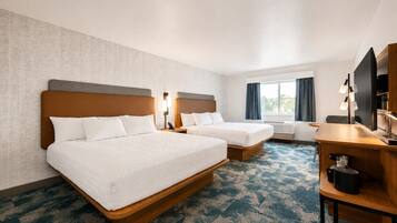 A hotel room with two beds, a desk, a TV, and a window with curtains.