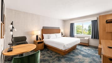 Een hotelkamer met een bed, nachtkastje, lamp, stoel, bureau en een raam met gordijnen.