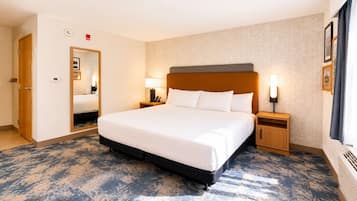 A hotel room with a large bed, bedside lamps, a mirror, and a carpeted floor.