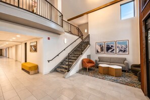 A spacious lobby with a staircase, a seating area with a sofa and chairs, and a patterned rug.